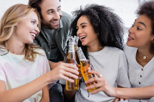 Happy man and joyful interracial women clinking bottles of beer — Stock Photo
