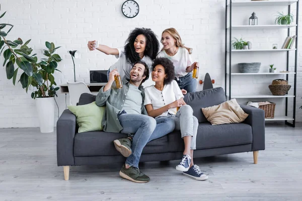 Feliz afroamericana mujer tomando selfie con amigos en sala de estar - foto de stock