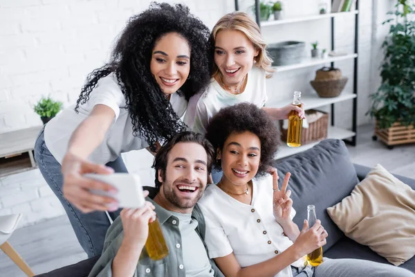 Happy african american woman taking selfie with cheerful friends in living room — Stock Photo
