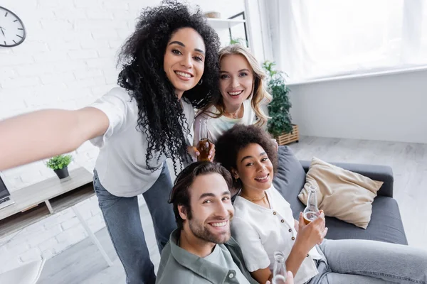 Glücklich afrikanisch-amerikanische Frau blickt in die Kamera mit fröhlichen Freunden im Wohnzimmer — Stockfoto