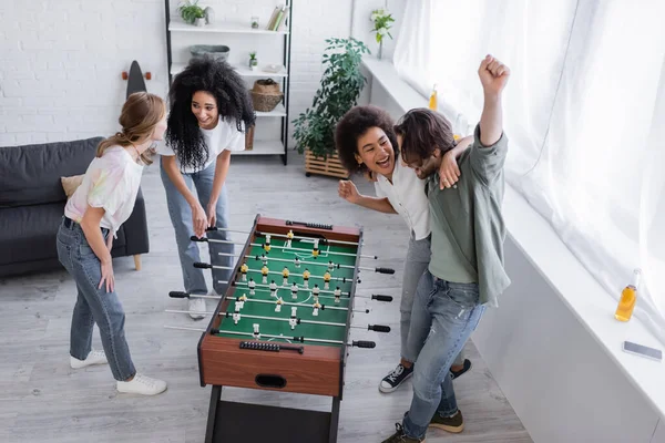 Alto ángulo vista de feliz interracial amigos regocijo cerca de futbolín - foto de stock