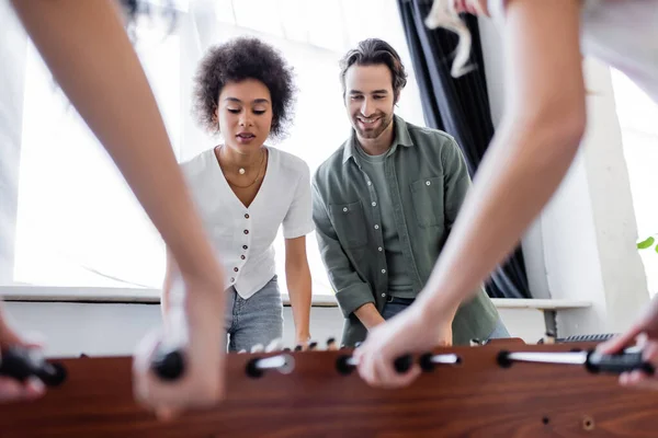 Interracial woman and man playing table football with blurred friends — Stock Photo