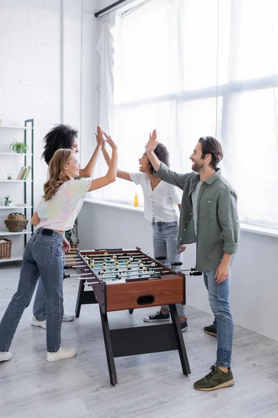 Happy interracial friends giving high five near table football — Stock Photo