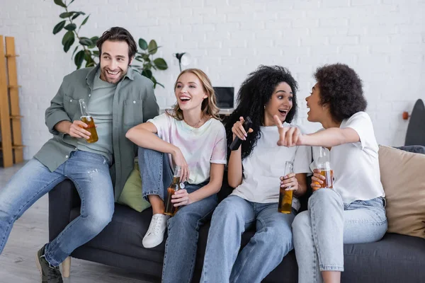 Mulheres americanas africanas felizes olhando umas para as outras perto de amigos sentados no sofá e assistindo filme — Fotografia de Stock