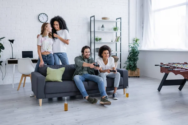 KYIV, UKRAINE - OCTOBER 7, 2021: focused multiethnic friends playing video game near happy lesbian couple — Stock Photo