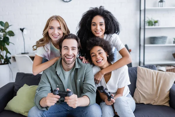 QUIIV, UCRÂNIA - OUTUBRO 7, 2021: mulheres multiétnicas felizes abraçando amigos jogando videogame na sala de estar — Fotografia de Stock