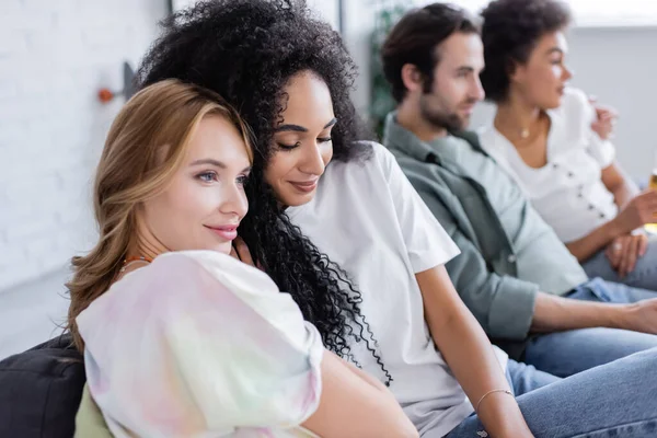 Cheerful lesbian women and blurred heterosexual couple sitting on sofa — Stock Photo