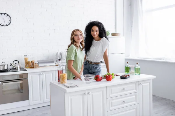 Веселая многонациональная лесбийская пара, стоящая вместе на современной кухне — стоковое фото