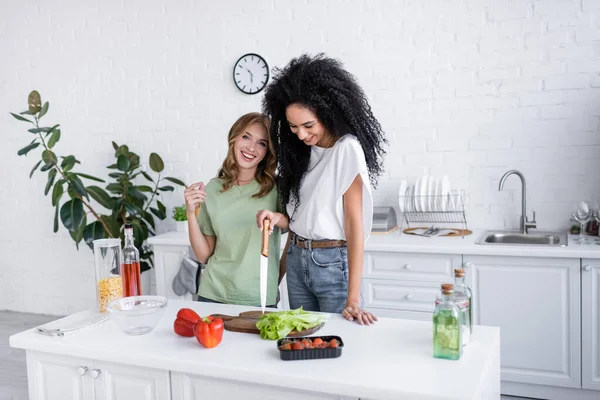 Heureux multiethnique lesbienne couple cuisine ensemble dans moderne cuisine — Photo de stock