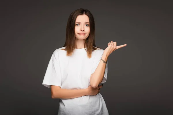Обескураженная женщина, смотрящая в камеру и указывая пальцем на темно-серый — стоковое фото
