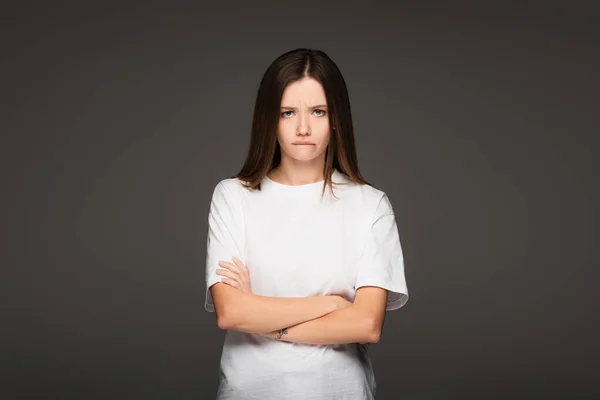 Femme offensée en t-shirt blanc debout avec les bras croisés isolés sur gris foncé — Photo de stock