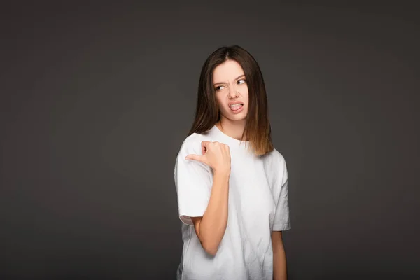 Young woman feeling disgusted, sticking out tongue and pointing with thumb isolated on dark grey — Stock Photo
