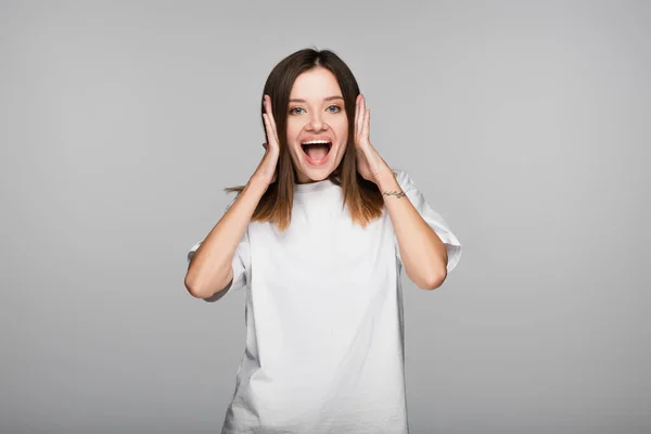 Astonished woman holding hands near head and shouting isolated on grey — Stock Photo