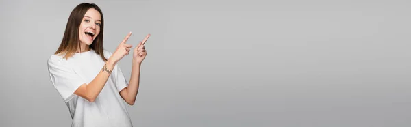 Astonished woman pointing with fingers while looking at camera isolated on grey, banner — Stock Photo