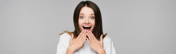 Thrilled woman with open mouth holding hands near face isolated on grey, banner — Stock Photo