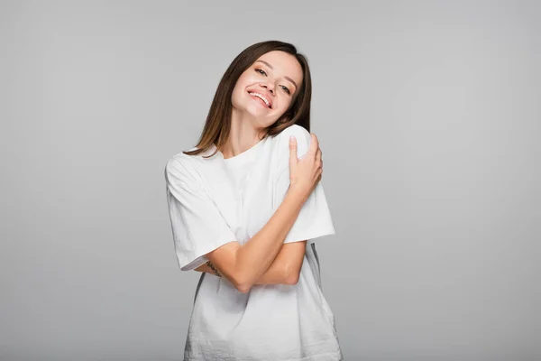 Mulher satisfeita em t-shirt branca abraçando-se isolado em cinza — Fotografia de Stock