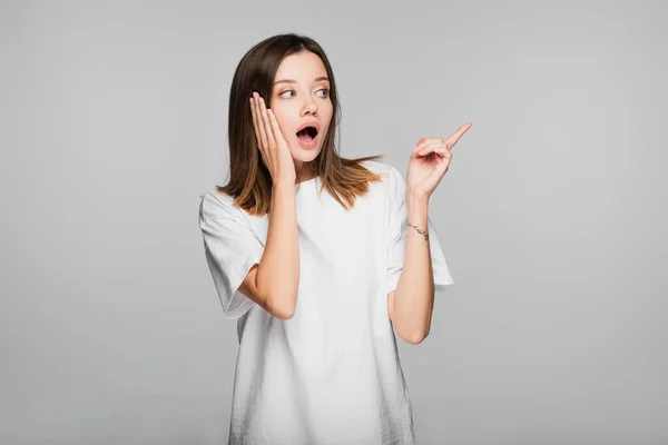 Shocked woman touching head and pointing with finger isolated on grey — Stock Photo