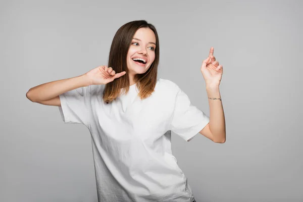 Femme souriante regardant loin et pointant les doigts isolés sur le gris — Photo de stock