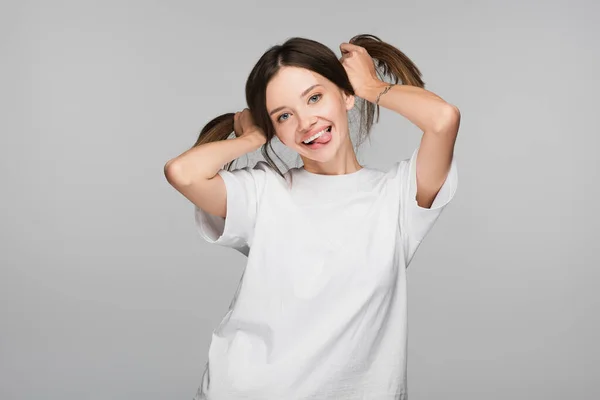 Excited and cheerful woman with ponytails sticking out tongue isolated on grey — Stock Photo