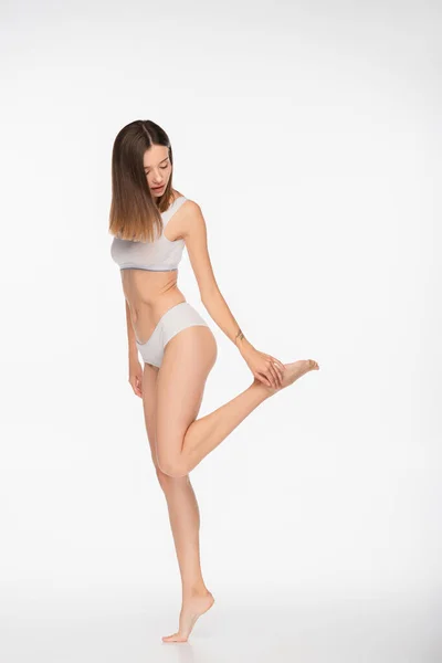 Comprimento total vista de mulher em forma de roupa interior tocando perna no fundo branco — Fotografia de Stock