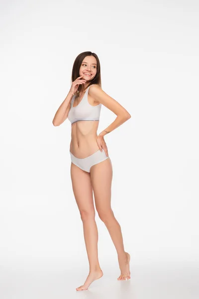 Femme heureuse en sous-vêtements regardant loin tout en se tenant avec la main sur la hanche sur fond blanc — Photo de stock