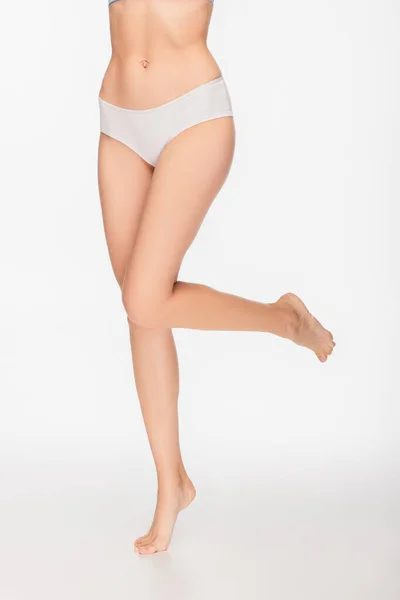 Partial view of barefoot woman in panties standing on one leg on white background — Stock Photo