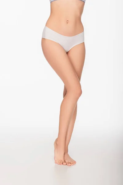 Частичный вид женщины с стройными и гладкими ногами, стоящей босиком на белом фоне — стоковое фото