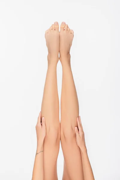 Vista recortada de la mujer tocando piernas descalzas delgadas aisladas en blanco - foto de stock