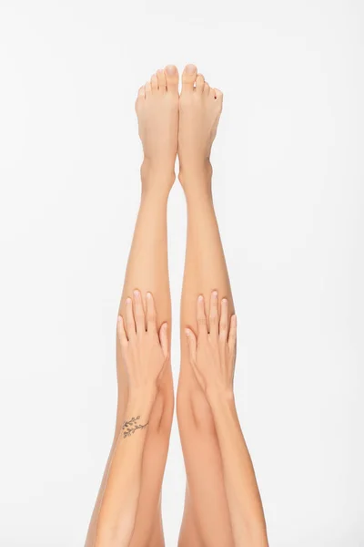 Частичный вид молодой женщины с татуированной рукой и тонкими ногами, изолированными на белом — стоковое фото