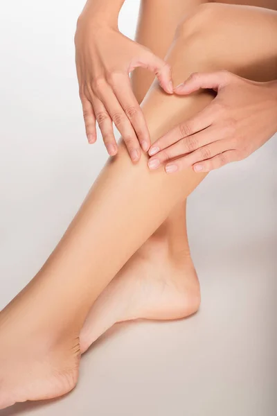 Vue recadrée de la jeune femme montrant signe cardiaque près des jambes avec une peau parfaite sur fond blanc — Photo de stock