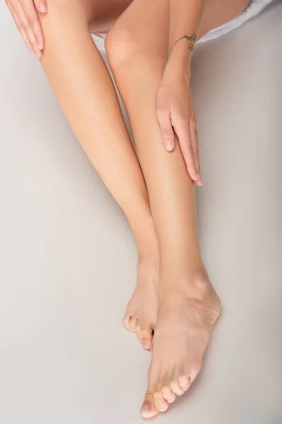 Abgeschnittene Ansicht einer barfüßigen Frau, die glatte Beine berührt, während sie auf weißem Hintergrund sitzt — Stockfoto