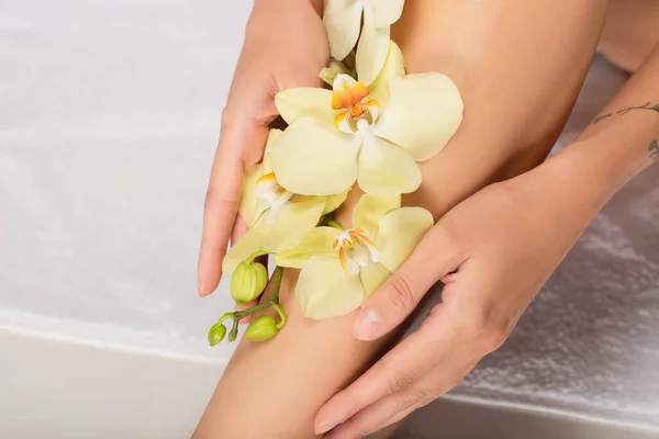 Abgeschnittene Ansicht einer Frau mit Orchidee auf glattem Bein, die auf weißem Handtuch sitzt — Stockfoto