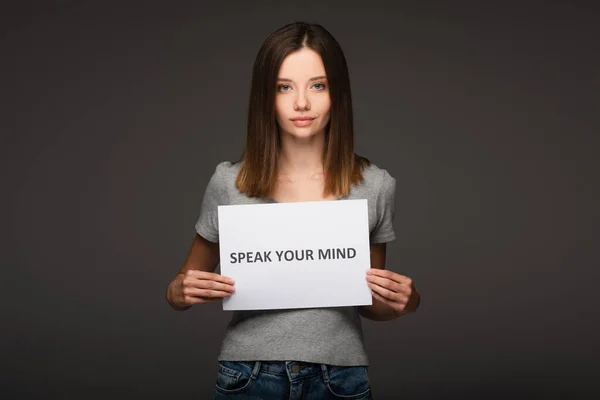 Young woman holding card with speak your mind phrase isolated on grey — Stock Photo