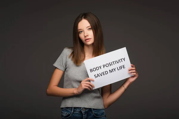 Morena mujer sosteniendo papel con cuerpo positividad salvó mi vida letras aisladas en gris - foto de stock