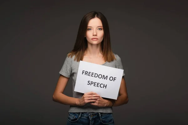 Молодая брюнетка с карточкой свободы слова, изолированная на сером — стоковое фото