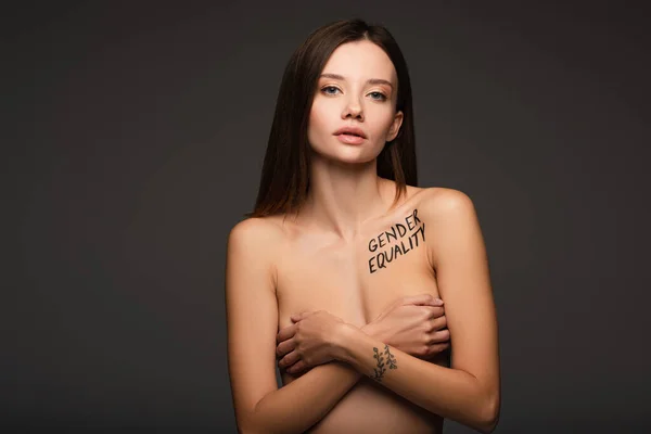 Nude woman with gender equality lettering on body hiding breast under hands isolated on dark grey — Stock Photo