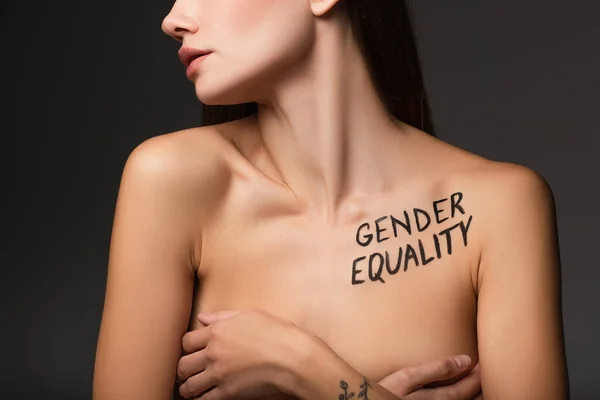 Partial view of young woman with gender equality inscription on body covering breast with hands isolated on dark grey — Stock Photo