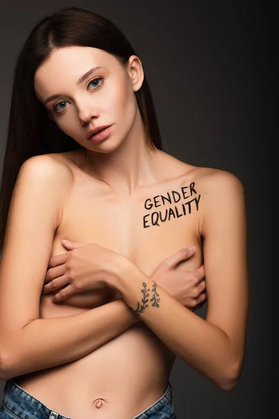 Brunette woman with gender equality phrase on body covering breast with hands isolated on dark grey — Stock Photo