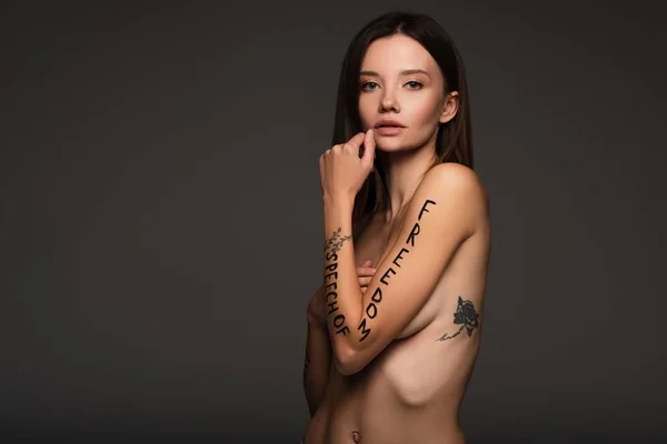 Nude and tattooed woman with freedom of speech phrase written on arm isolated on dark grey — Stock Photo