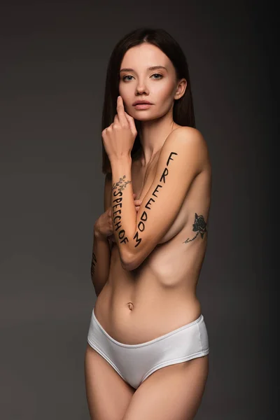 Стройная женщина с татуировкой и надписью свободы слова на теле, изолированном на темно-сером — стоковое фото