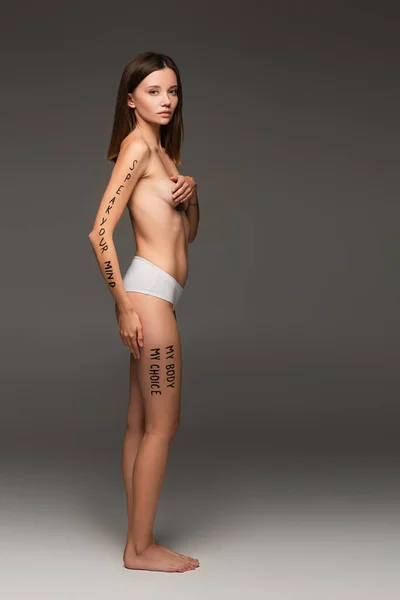 Full length view of woman in panties, with slogans written on body isolated on dark grey — Stock Photo