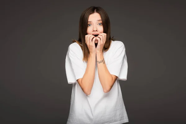 Shocked and scared woman holding hands near open mouth isolated on dark grey — Stock Photo