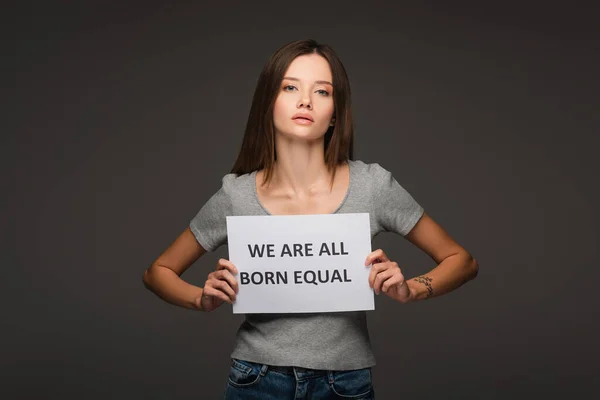 Joven morena mujer sosteniendo pancarta con todos nacemos iguales letras aisladas en gris - foto de stock