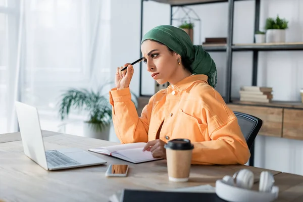 Pensive muslim woman looking at notebook while learning at home — Stock Photo