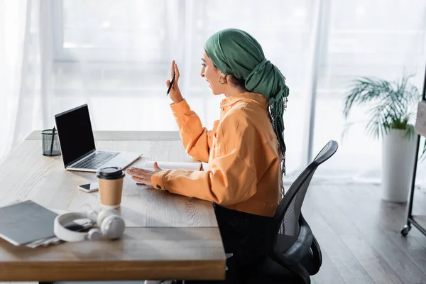 Vista laterale della donna musulmana che agita la mano durante la videochiamata sul computer portatile — Foto stock