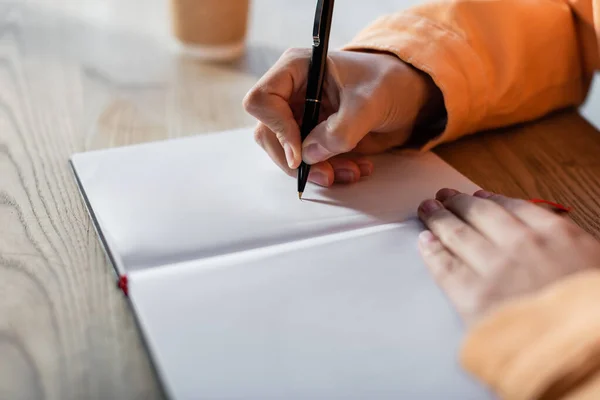 Teilansicht eines Schülers, der zu Hause auf ein leeres Notizbuch schreibt — Stockfoto