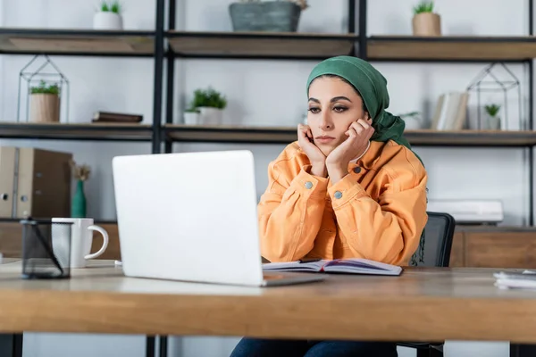 Arabian woman in headkerchief sitting with hands near face during online lesson on laptop — Stock Photo