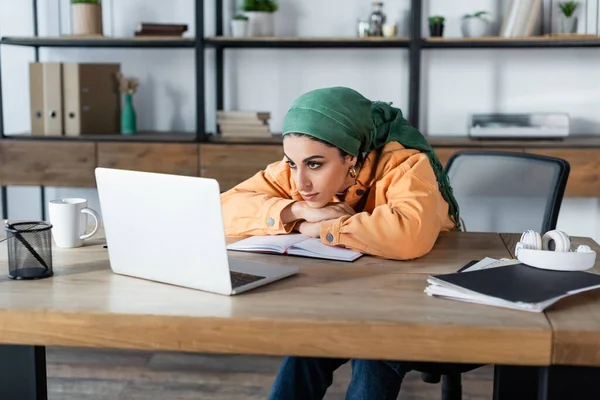 Jovem mulher muçulmana olhando para laptop durante webinar em casa — Fotografia de Stock