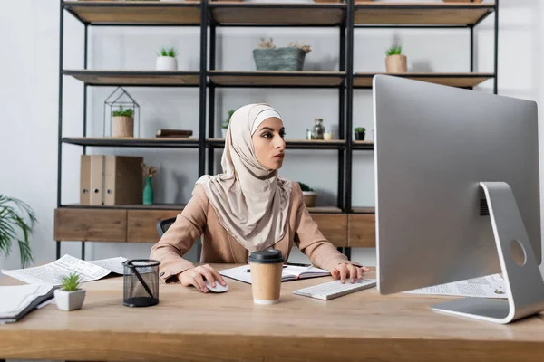 Jeune femme arabe en hijab travaillant sur ordinateur près du café pour aller à la maison — Photo de stock