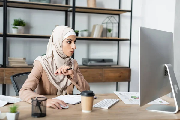 Giovane donna araba che lavora su computer vicino notebook e bevande da asporto sulla scrivania — Foto stock